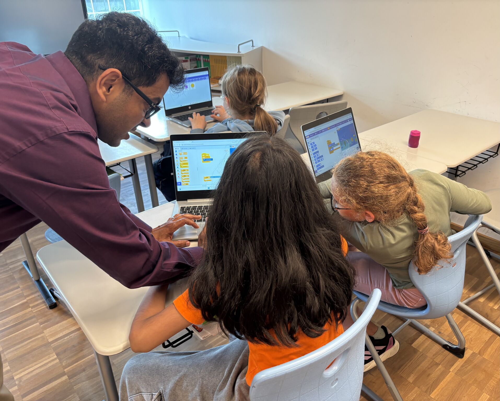 Coach aidant trois jeunes à coder en Scratch sur leur ordinateur portable